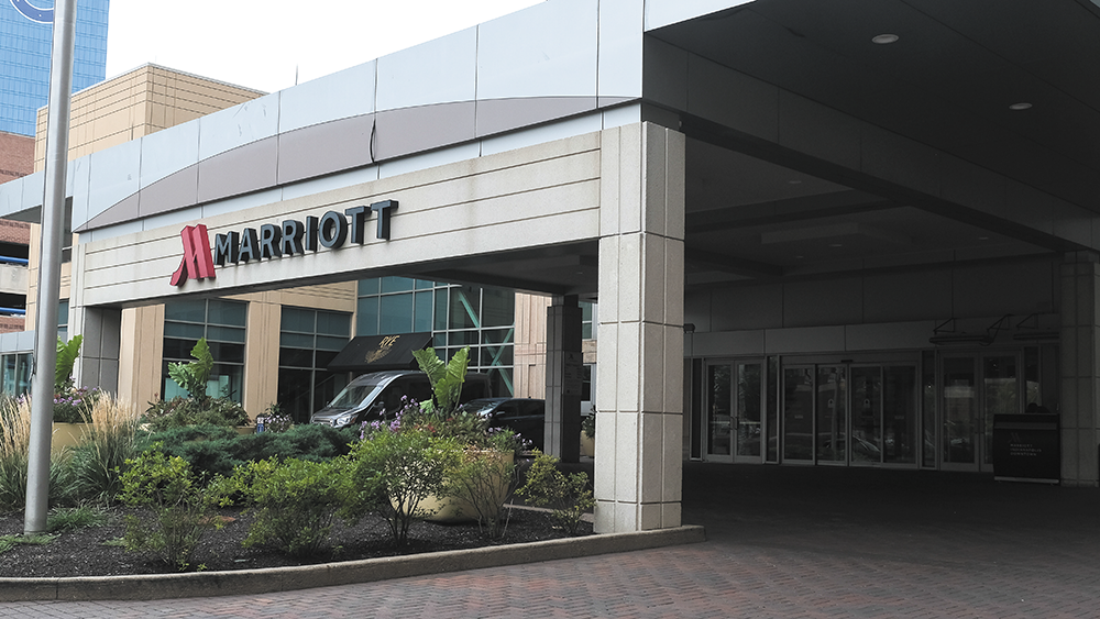 Photograph of a large porte-cochère with a sign that reading Marriott. In front of the pavement is a manicured garden bed. 